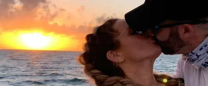 a man and a woman kissing with a sunset in the background.